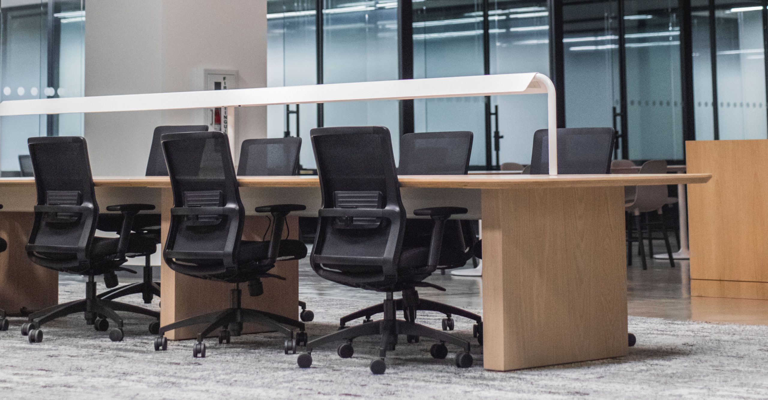 A modern office space designed to boost employee productivity features a long wooden table and black office chairs in front of large windows.