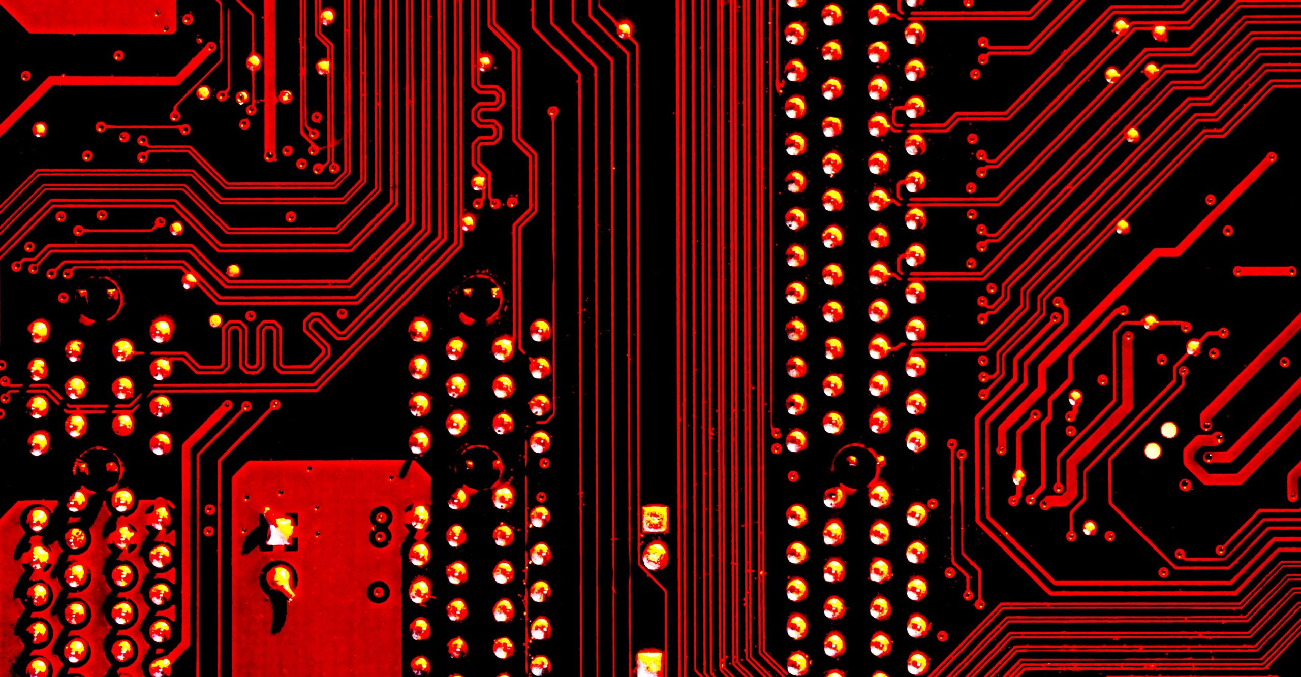 Close-up of a red and black printed circuit board showing intricate pathways and numerous small metallic components, illustrating how to paste electronic parts precisely.