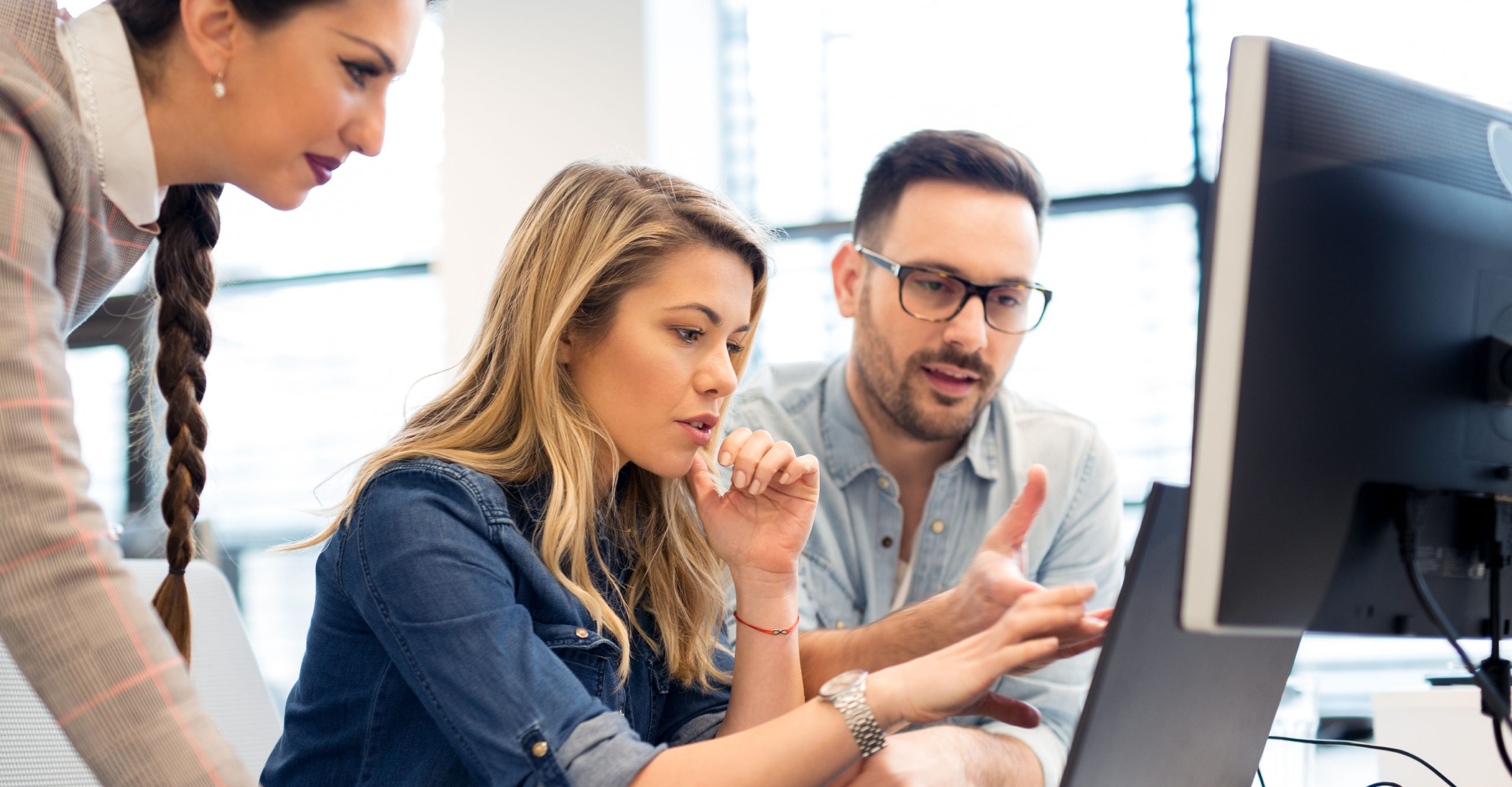 Three people are gathered around a computer, engaged in a discussion. One person is pointing at the screen while the others observe attentively, immersed in their cyber training session.