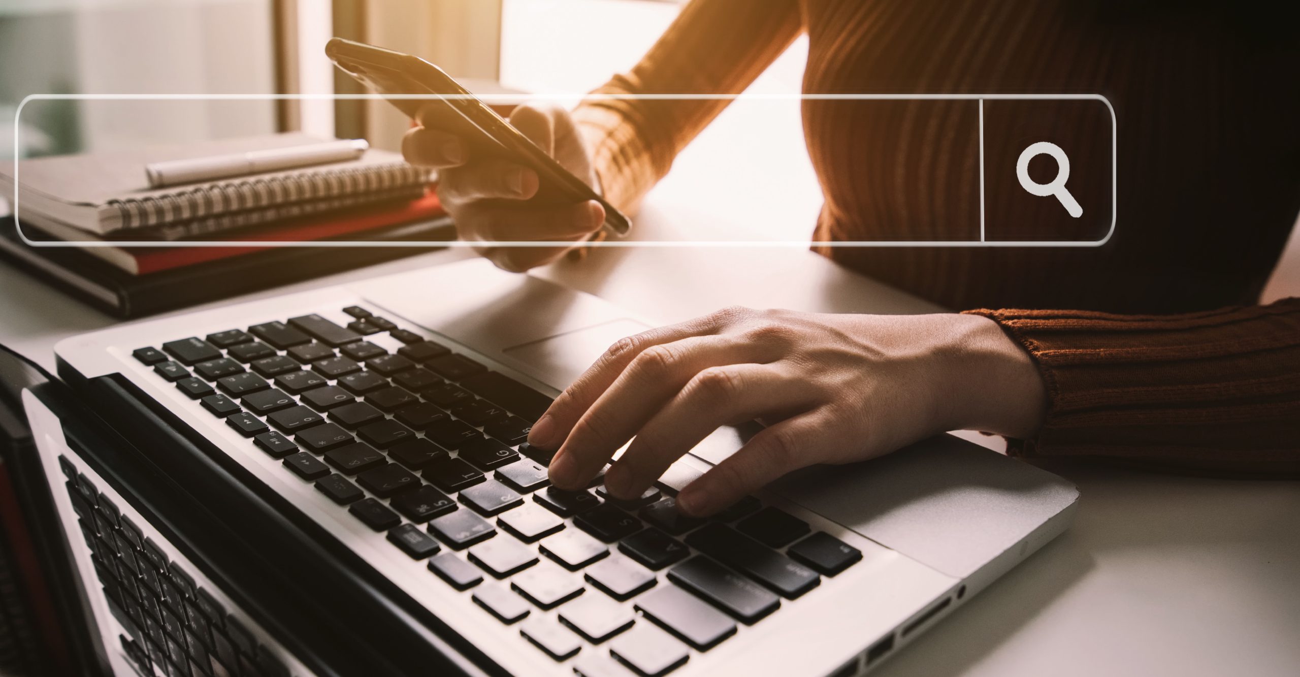 Person typing on a laptop while holding a smartphone, with a search bar graphic overlay, seamlessly navigating server management tasks.