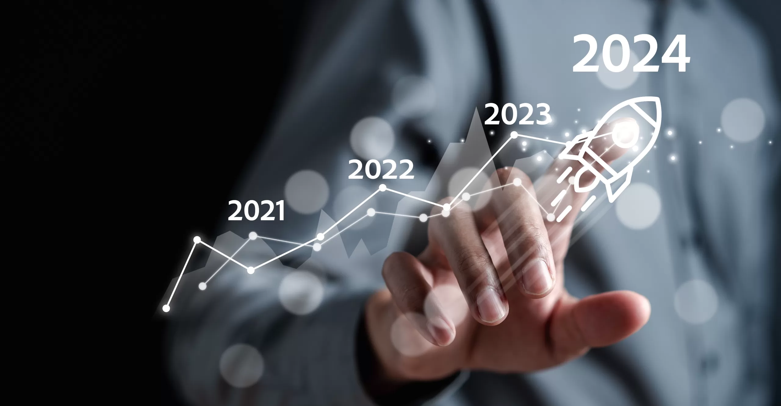 A person points to a rocket icon near "2024" on a graph, with previous years "2021," "2022," and "2023" leading up to it. The graph shows an upward trend, reflecting the impact of systems hardening efforts over time.