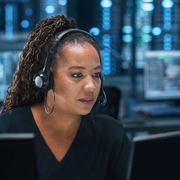 A woman wearing a headset works at a computer in an office with multiple screens, providing network support in the realm of managed IT services.